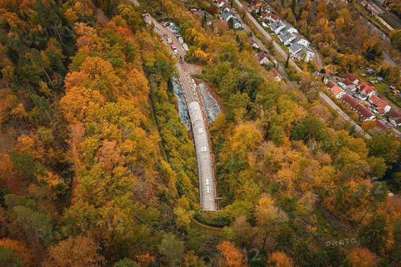 Aerial view of a railway tunnel surrounded by autumnal forest and nearby houses, Hermann Hesse Railway bat tunnel construction site, Calw, Black Forest, Germany