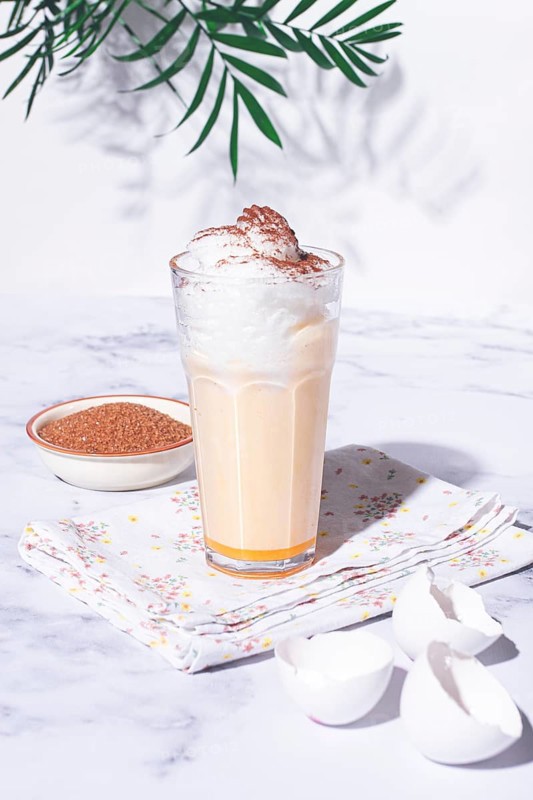 Eggnog drink, egg yolk, in a glass, with cream and cinnamon, sunlight