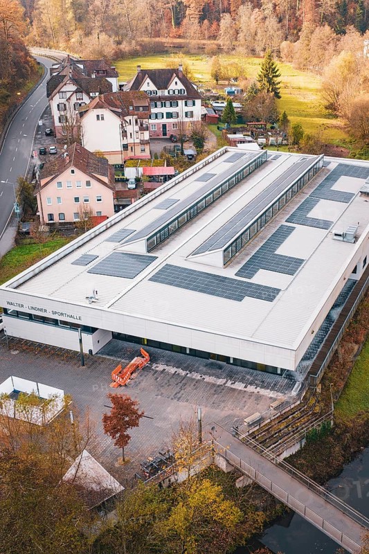 Building with solar panels surrounded by village houses and autumn trees, PV at Walther Lindner Sporthalle Calw, Black Forest, Germany