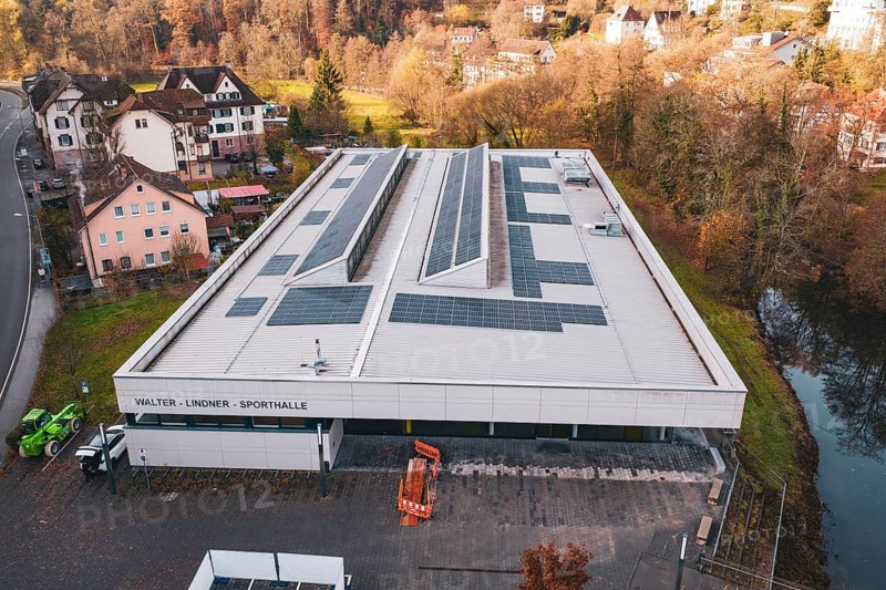 Building with solar systems in a rural environment, near a river, PV at Walther Lindner Sporthalle Calw, Black Forest, Germany