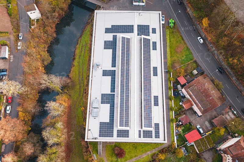 Aerial view of a building with solar panels, surrounded by river and roads, PV at Walther Lindner Sporthalle Calw, Black Forest, Germany