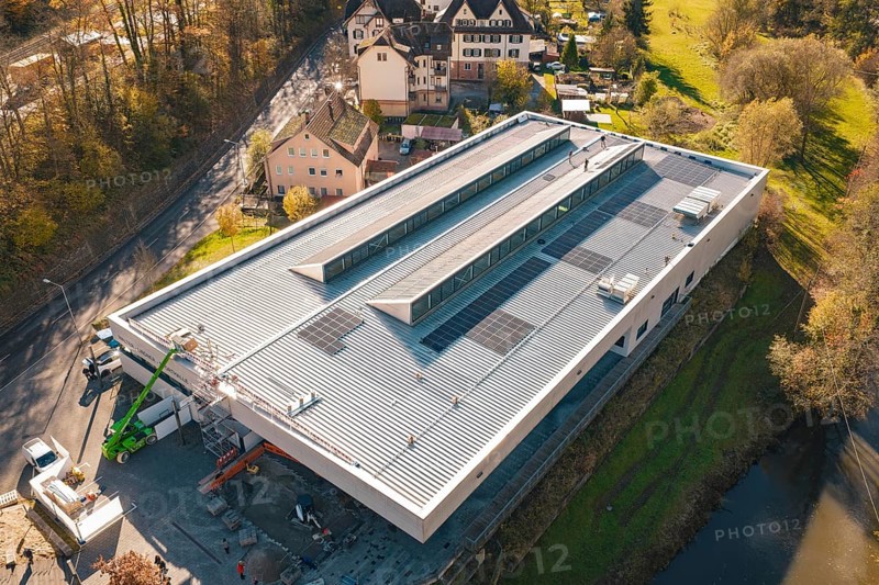 Modern building with solar panels, surrounded by a river and autumnal nature, viewed from the air, PV at Walther Lindner Sporthalle Calw, Black Forest, Germany