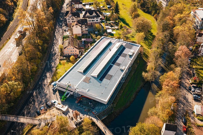 Bird's eye view of a modern building with solar cells, nestled in an autumnal village and river landscape, PV at Walther Lindner Sporthalle Calw, Black Forest, Germany