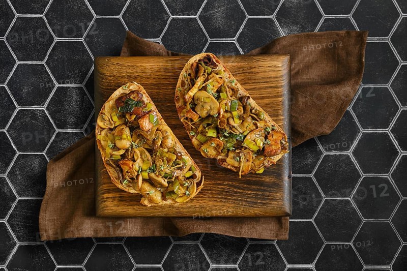 Two sandwiches with flavorful mix of honey mushrooms, enoki mushrooms, champignon, and leeks. Perfectly presented on a wooden board with a stylish background, inviting a tasty experience