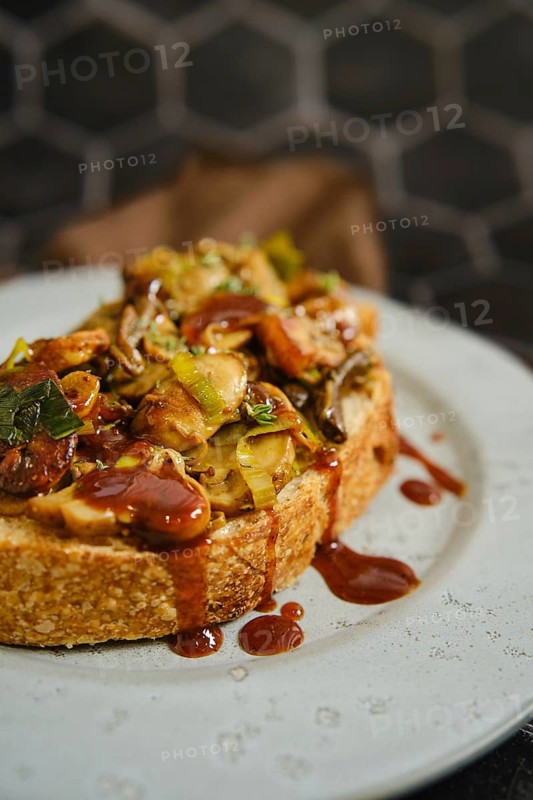 A warm mushroom sandwich is served on a rustic plate, topped with honey mushrooms, enoki mushrooms, champignon, and fresh leek