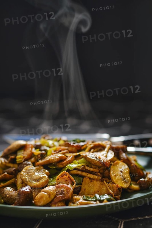 A colorful mix of mushrooms and vegetables is stir-fried to perfection, filling the air with delicious aromas. The dish steams gently as it is presented on a dark-colored plate