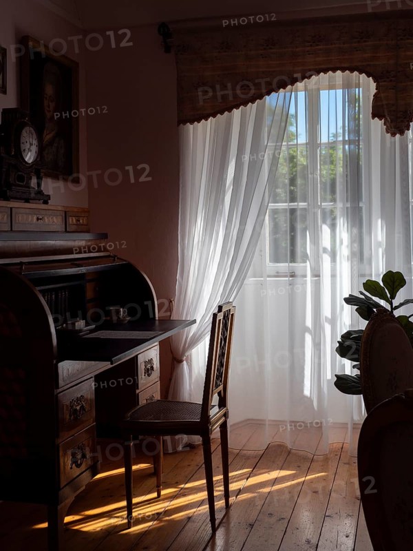 White tulle curtains in antique room with old secretary furniture and chair