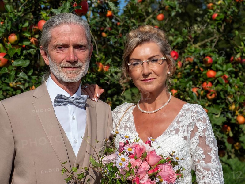 Elderly couple's wedding, look in front of a tree with lots of red apples