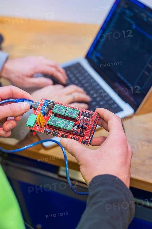 Person holding circuit board while someone is programming on a laptop, Jugend Forschungszentrum Nagold, Landkreis Calw, Germany