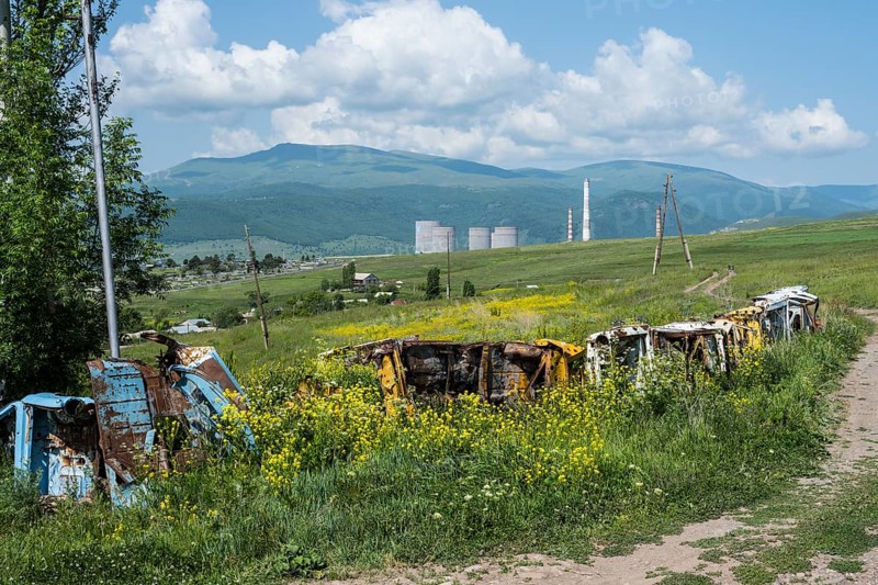 Rusty vehicles stand in a meadow in front of a wooded mountain panorama, scrap cars serve as a fence near Zovaber, Kotayk province, Armenia