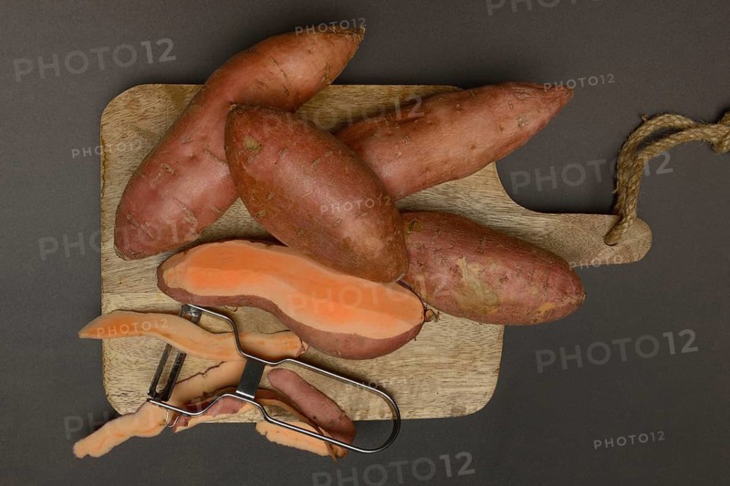 Sweet potatoes with potato peeler on wooden board, Ipomoea batatas