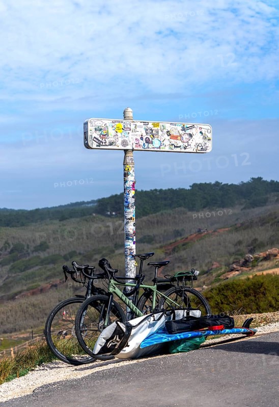 Sticker-covered sign with bicycles and surfboards, Nazaré, Portugal