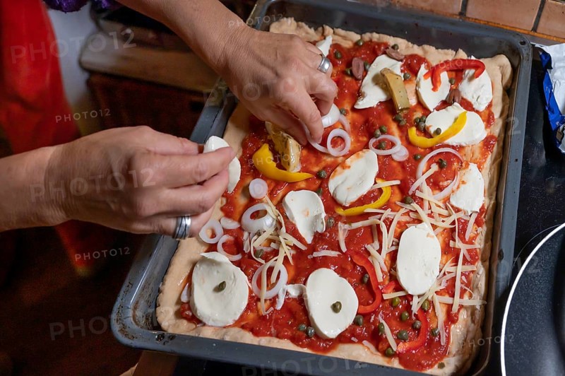 Topping a homemade pizza, gorgonzola and tomatoes, olives and parika on a baking tray, Othenstorf, Mecklenburg-Western Pomerania, Germany