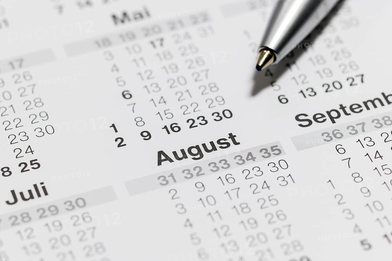 Close-up of a calendar with ballpoint pen pointing to the month of August