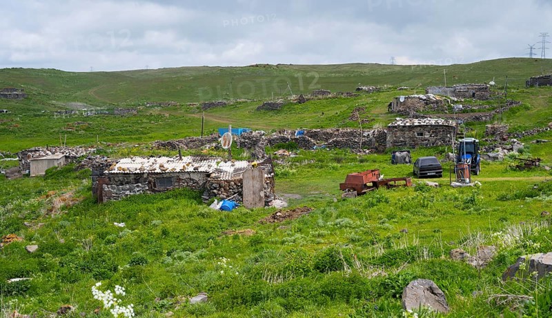 Rural town with dilapidated buildings and green fields under cloudy sky, small town on the M10 near Nshkhark, Gegharkunik province, Armenia