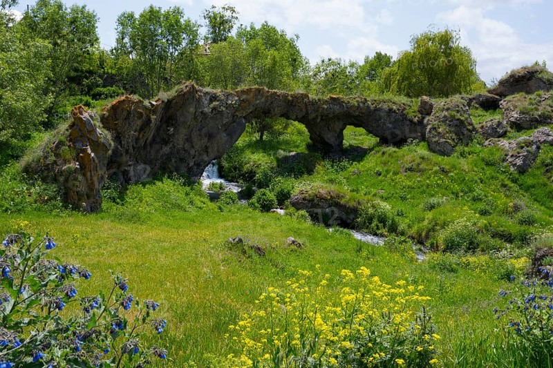 Landscape with natural rock arch, green vegetation and flowing stream, Tsakkar bridge in the village of Tsakkar, Gegharkunik province, Armenia