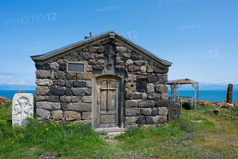 Stone chapel with wooden door in the foreground, sea in the background under clear sky, Chapel of the Holy Cross, Sarukhan, Lake Sevan, Gegharkunik Province, Armenia
