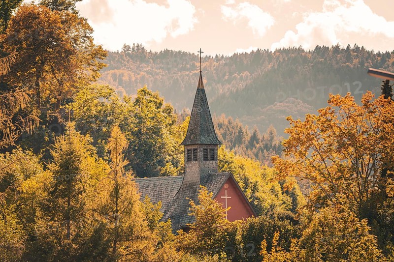 An idyllic church nestled in autumn leaves in front of a mountain landscape