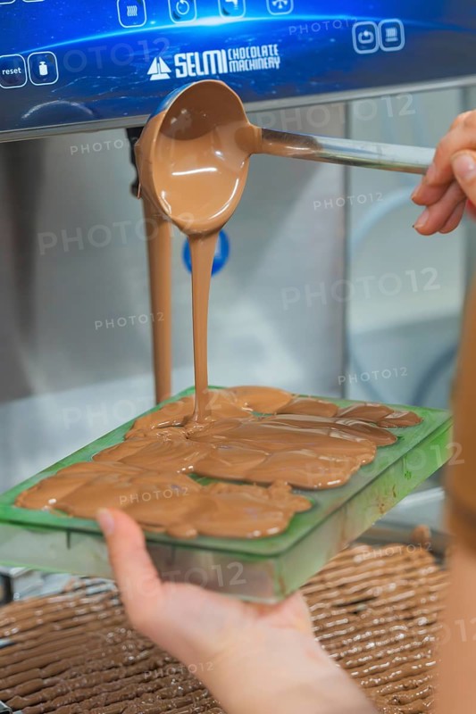 Hand pouring warm chocolate from a ladle into chocolate molds, Christmas baking, Haselstaller Hof, Wildberg, Calw district, Germany