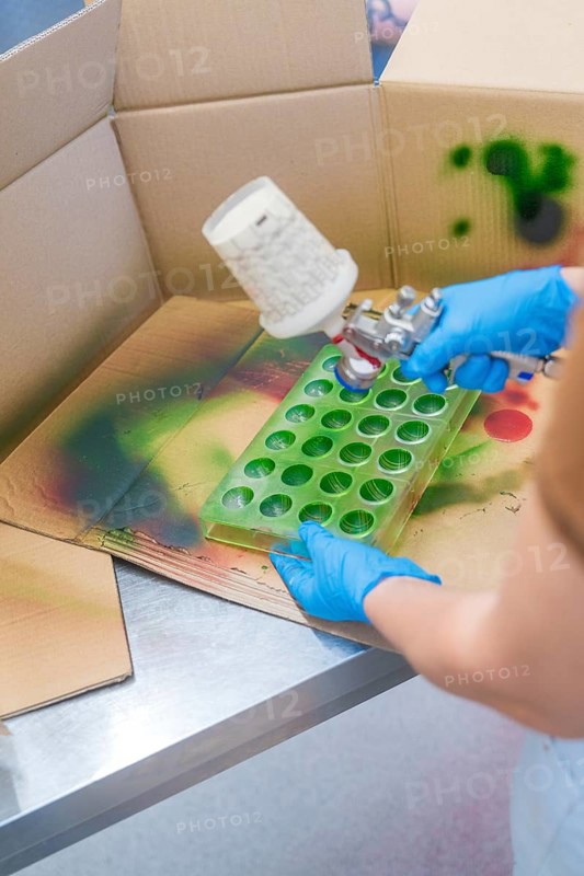 Person spraying green paint into a recessed mold on a cardboard table, Christmas baking, Haselstaller Hof, Wildberg, Calw district, Germany