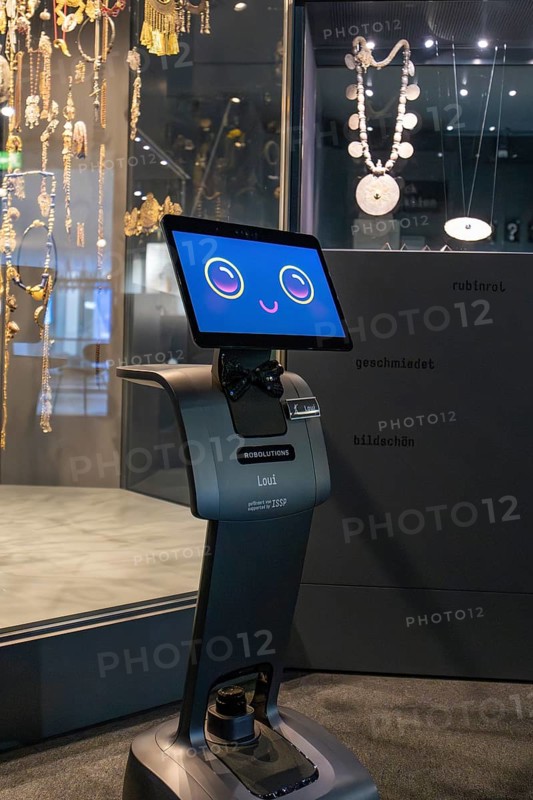 Robot with smiling display stands in front of a jewelry exhibition in the museum, robot personality Roboloutions in the jewelry museum, Pforzheim, Germany