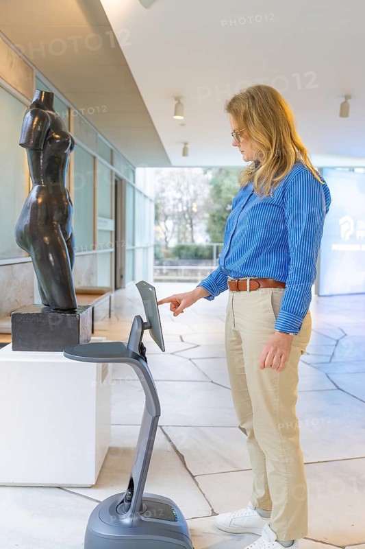 Woman interacting with a device in front of a statue in a modern setting, robotic personality Roboloutions in the jewelry museum, Pforzheim, Germany