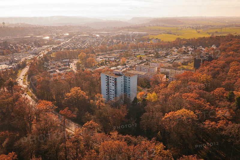 A residential building towers over an autumnal forest with a town behind it, MÃ¼hlacker, Enzkreis, Germany