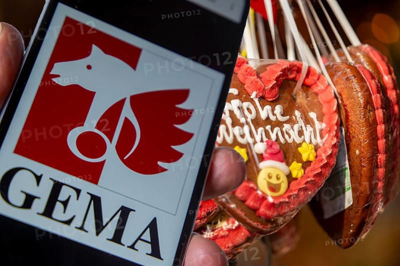 (photo montage) Smartphone with opened GEMA logo in front of a stand at a Christmas market