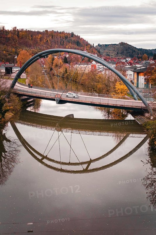 Bridge with arched design reflecting in calm river water surrounded by autumn trees, Sulz am Neckar, Germany