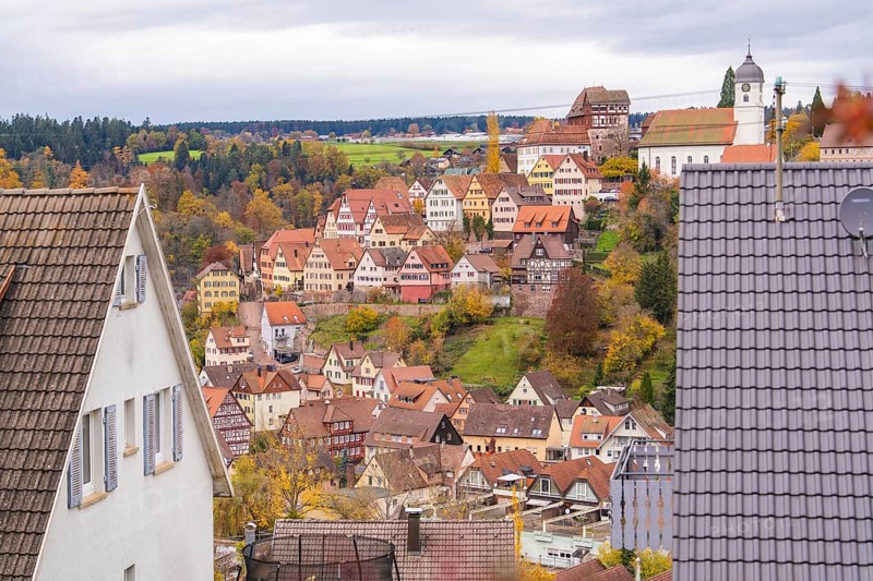 City view with visible church tower and half-timbered houses surrounded by autumn leaves on a hill, Altensteig, Calw district, Germany