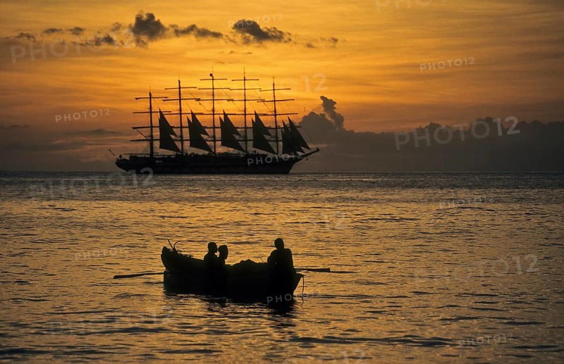Romantic view of the Caribbean Sea during sunset In the foreground small fishing boat with three local fishermen heading out to sea for fishing at dusk, tall ship five-master sailing ship Royal Clipper, Caribbean