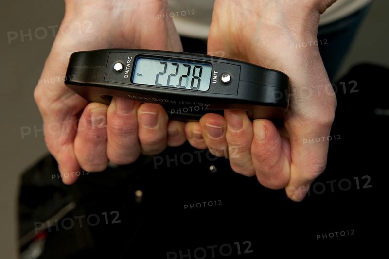 Woman holding hand scale for weight of suitcase travel bag flight luggage checks luggage weight for excess luggage weight in front of flight travel, scale shows 22.28 kg kilos, international