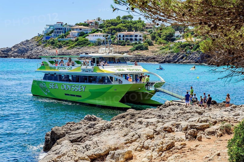 Tourists get on board a glass-bottom boat docks at the small bay Font de Sa Cala on the east coast of the Balearic island of Majorca in the Mediterranean Sea, Majorca, Balearic Islands, Spain