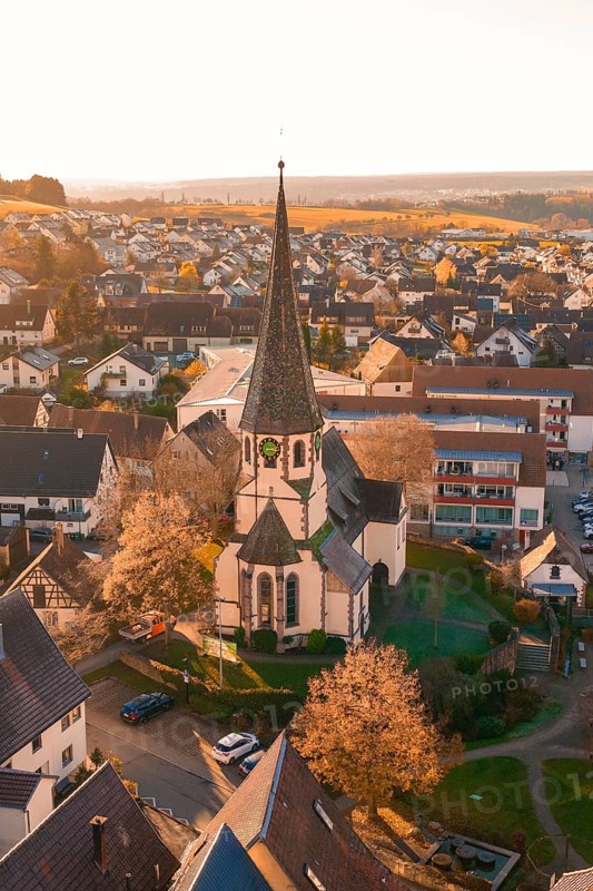 Bird's eye view of a village with a church in the center, surrounded by blooming trees and houses in the evening light, Althengstett, Calw district, Germany