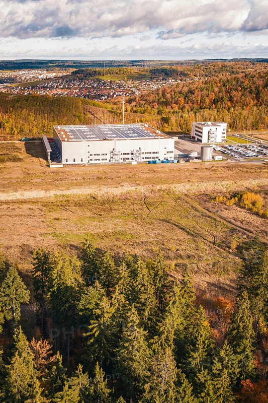 Factory building next to forest and clearing, behind a village on a hill in autumn tones, new Lindenrain industrial park, Calw, Black Forest, Germany