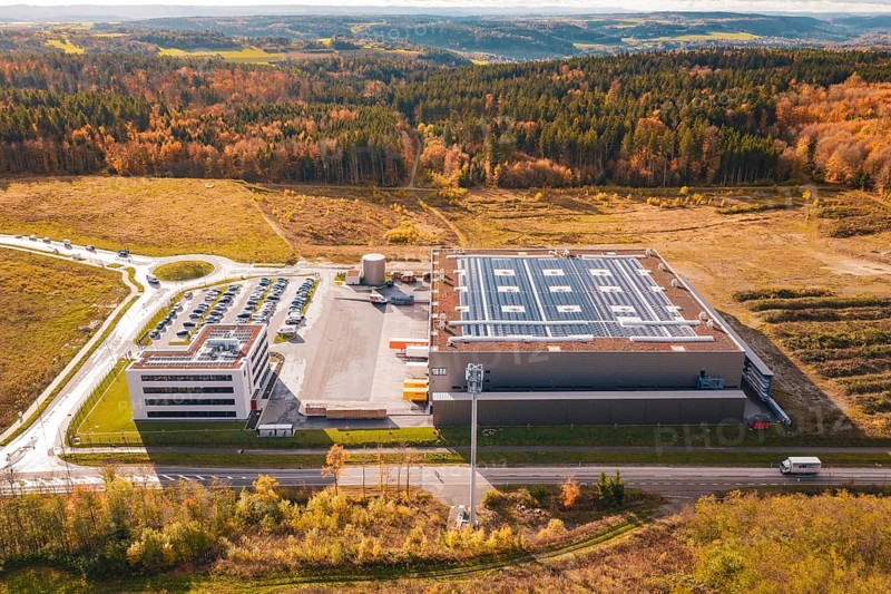 Large factory with parking lot, surrounded by forest and open spaces in an autumnal setting, new Lindenrain industrial park, Calw, Black Forest, Germany