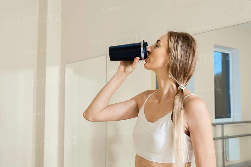 Woman enjoying a drink while standing in a fitness studio after a workout session