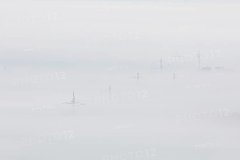 High-voltage pylons rise up from the thick sea of fog, silence and technology the silhouette of power lines in fog