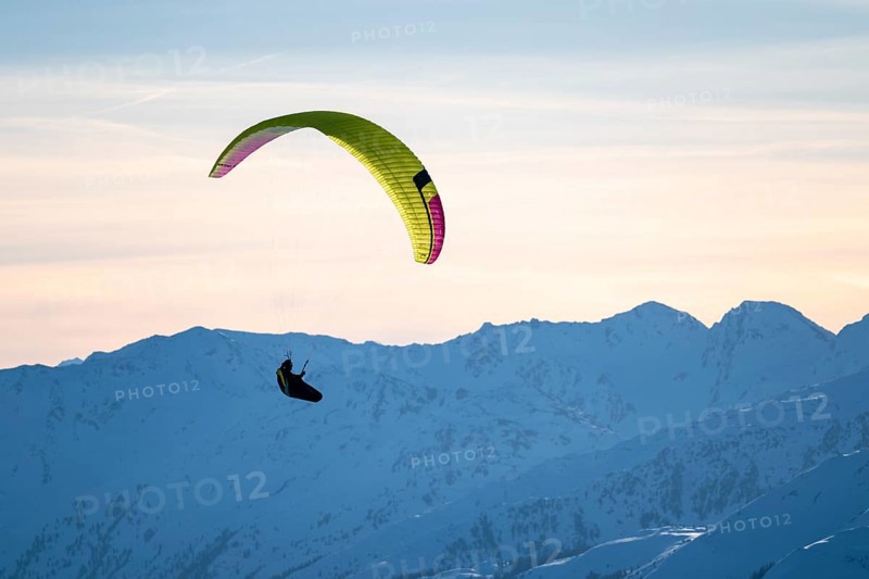 Paragliders flying over snowy mountain peaks in winter in evening light, KitzbÃ¼hel Alps, Tyrol, Austria