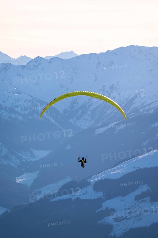 Paragliders flying over snowy mountain peaks in winter in evening light, KitzbÃ¼hel Alps, Tyrol, Austria