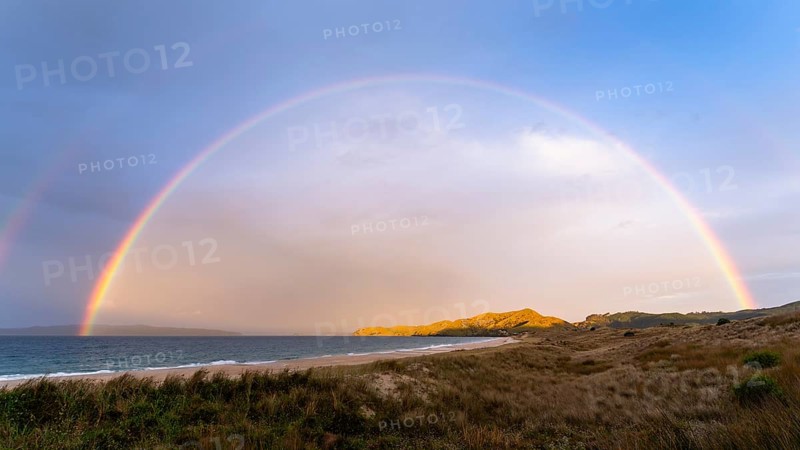 Landscape with sea and sandy beach in New Zealand with rainbow, in the evening at golden hour. Otama Beach, Coromandel Peninsula, Waikato, New Zealand