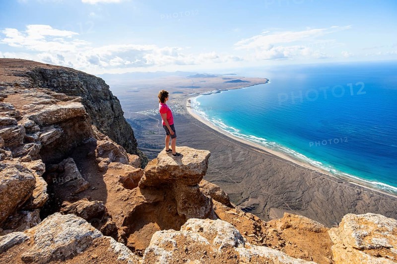 Woman enjoying the view from the Risco de Famara cliffs on Famara beach, Playa de Famara with La Calaeta, Lanzarote, Canary Islands, Spain