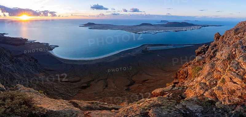 View of steep cliffs to sea and the island of La Graciosa with sun stars, Mirador del Porrito viewpoint at sunset, Lanzarote, Canary Islands, Spain