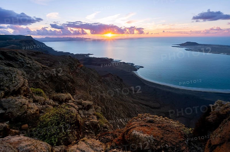 View from steep cliffs to sea and coast with sun stars, Mirador del Porrito viewpoint at sunset, Lanzarote, Canary Islands, Spain