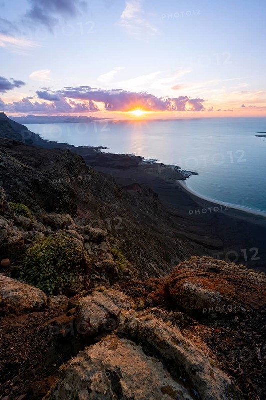 View from steep cliffs to sea and coast with sun stars, Mirador del Porrito viewpoint at sunset, Lanzarote, Canary Islands, Spain