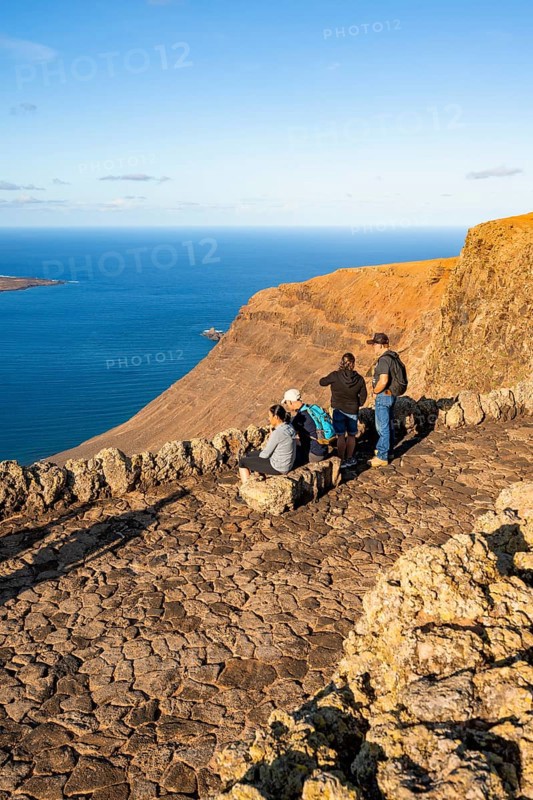 Tourists sitting on a bench on the observation deck at the Mirador del RÃ­o viewpoint, in the evening light, view of the sea and the steep cliffs, designed by artist César Manrique, Lanzarote, Canary Islands, Spain