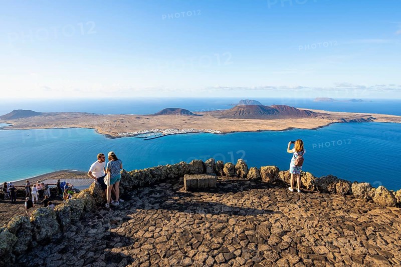 Tourists on the viewing platform at the Mirador del RÃ­o viewpoint, in the evening light, view of the sea and of the island of La Graciosa with volcanic craters, designed by artist César Manrique, Lanzarote, Canary Islands, Spain