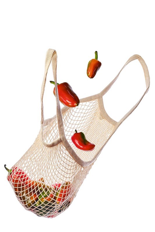 Colourful sweet bell peppers fall into an eco-friendly string bag isolated on white background