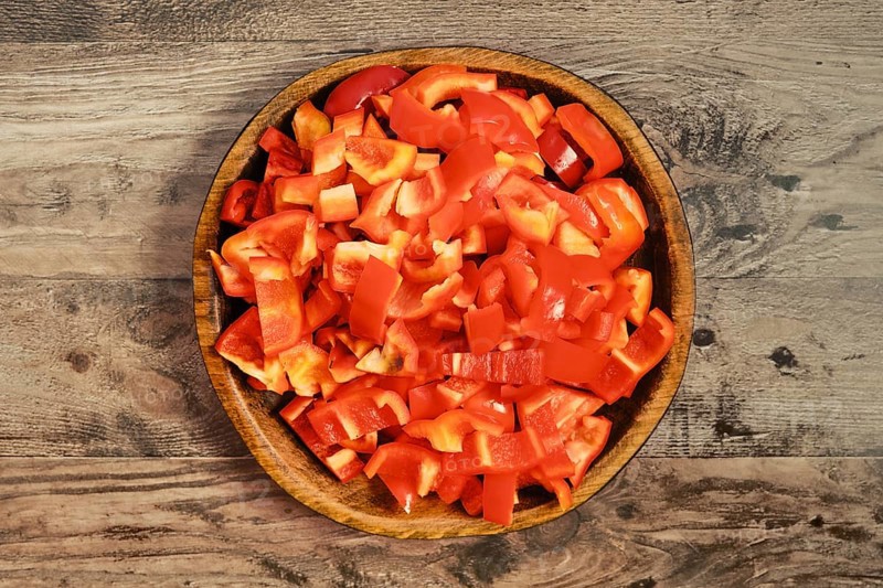 Freshly chopped red bell peppers in a wooden bowl. The chopped pieces are neatly arranged, ready to be used in various dishes