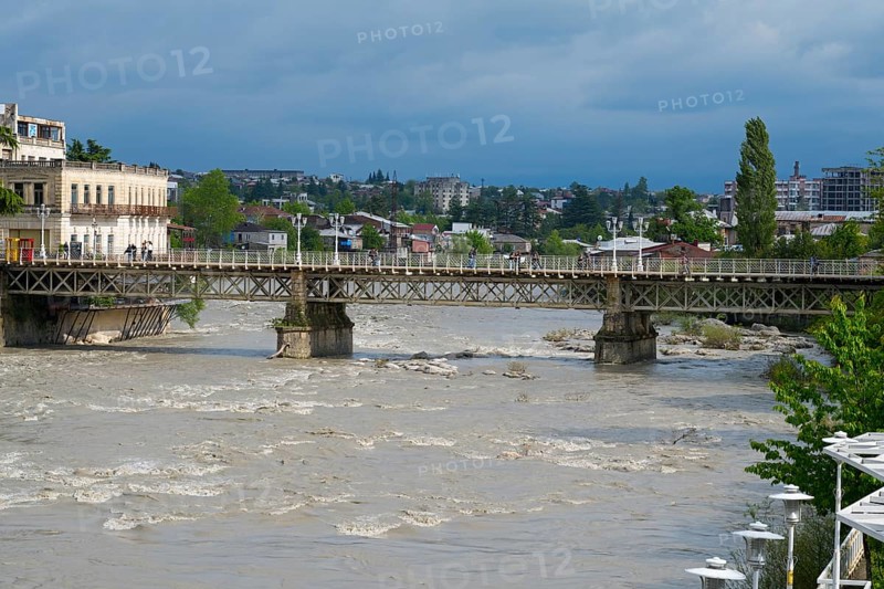A rustic bridge across a river with an urban backdrop under cloudy sky, White Bridge over the Rioni River, Kutaisi, Imereti Region, Georgia